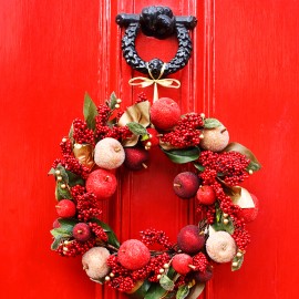 decorative Christmas wreath tied to knocker on red door